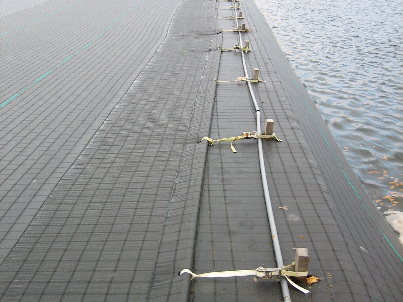 Tensioned cover mounted on a water reservoir anchored at the crest of the dike